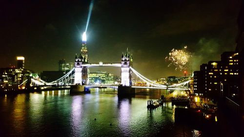 Illuminated bridge over river with city in background