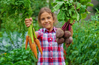 Portrait of girl holding carrot and beet at farm