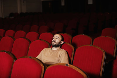 Man looking away while sitting on chair in theater