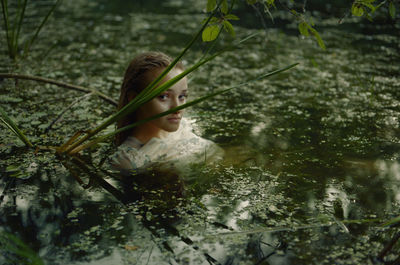 A woman in a white dress on the surface of a swamp water in the forest