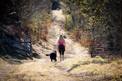 Rear view of woman with dog walking in forest