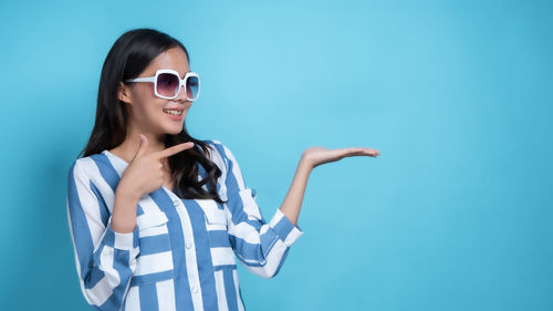 Young woman wearing sunglasses standing against blue background