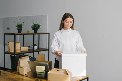 A cute girl is standing in the office with a large white paper box near the desk