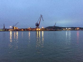 Cranes at harbor against sky at dusk