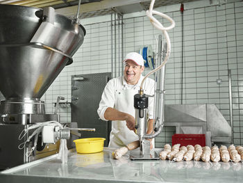 Happy butcher making sausages through machinery at factory