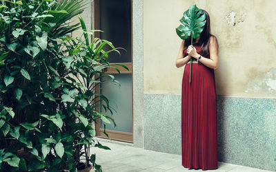 Woman holding leaf while standing against wall