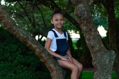 Portrait of smiling girl sitting on tree trunk