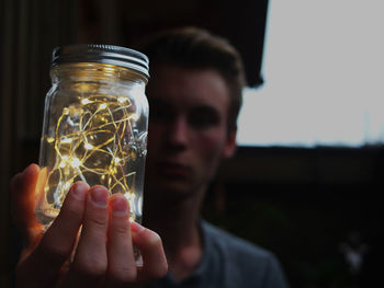 Young man holding illuminated lighting equipment in glass jar at dusk