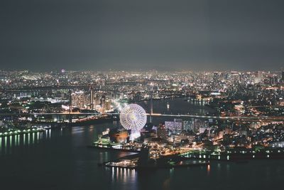 Illuminated cityscape by river against sky at night