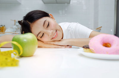 Smiling young woman lying on table with apple and donut