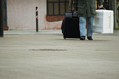 Low section of man with luggage walking on road