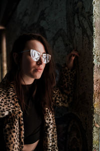 Portrait of woman wearing sunglasses standing against wall