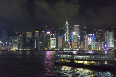 Illuminated buildings by river against sky at night