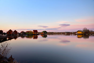 Scenic view of river by buildings against sky during sunset