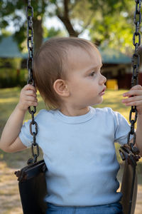 Girl playing in park hammock while watching other children playing