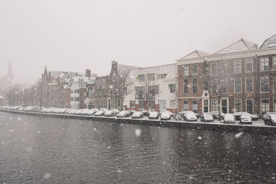 River by buildings against sky during snowfall
