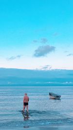 Rear view of man standing at beach against blue sky