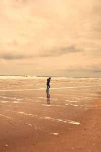 Mid distance view of woman walking on shore at beach against sky