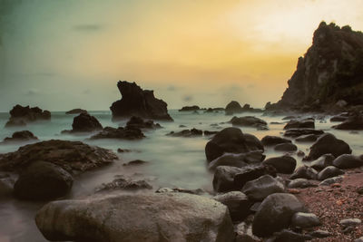 Rocks on beach against sky during sunset
