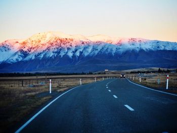 Road by mountains against clear sky during winter