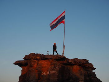 Low angle view of man standing on rock against sky