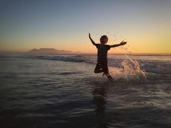 Boy with arms outstretched at beach during sunset