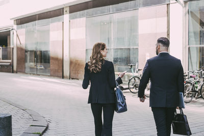 Rear view of businesswoman and businessman walking in city