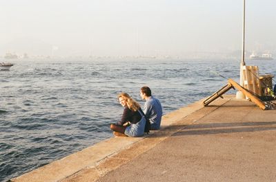 Young couple sitting on pier over sea