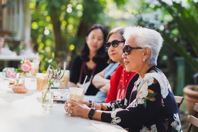 Asian senior woman and adult daughter drinking coffee at cafe outdoor.