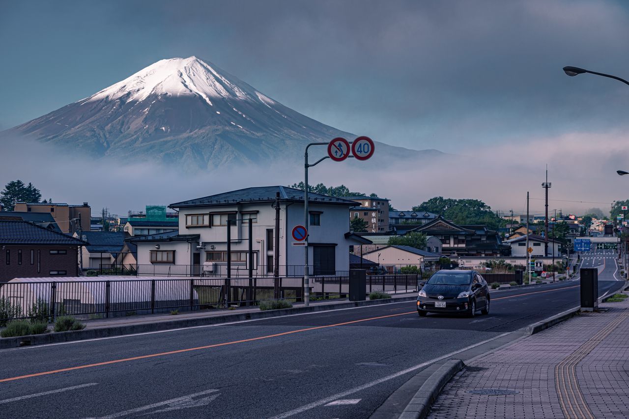 transportation, mountain, building exterior, sky, road, city, cloud - sky, built structure, architecture, mode of transportation, street, sign, land vehicle, motor vehicle, car, nature, volcano, symbol, dusk, building, no people, outdoors, snowcapped mountain, mountain peak