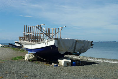 Abandoned ship moored on beach against sky