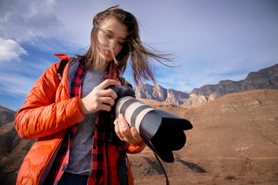 Young hipster woman with a camera in her hands in the mountains in backlight. hair fluttering 