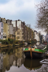 Boats moored in canal by buildings against sky