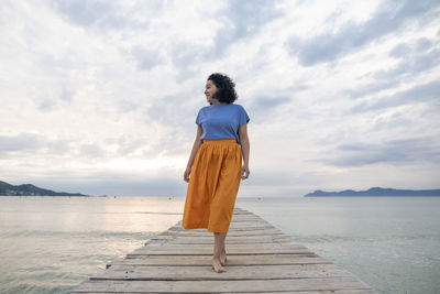 Thoughtful woman walking on jetty in front of sky