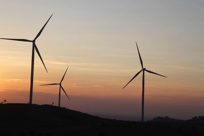 Silhouette wind turbines on field against sky during sunset