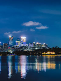 Illuminated buildings by river against sky