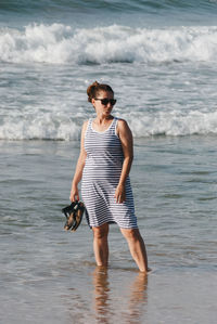 Woman holding sandals while standing on shore at beach