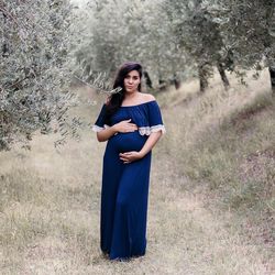 Portrait of pregnant woman touching abdomen while standing on grass