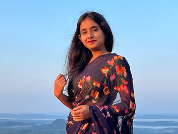 Portrait of young woman standing against sky