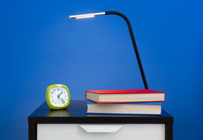 Low angle view of illuminated lamp on table against blue wall