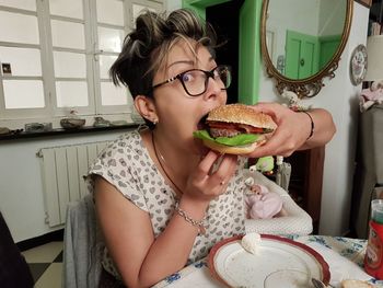 Portrait of woman eating burger while sitting at table