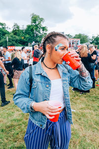 Young woman drinking drink while standing in city during party