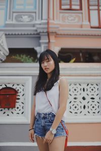 Portrait of smiling young woman standing against building in city