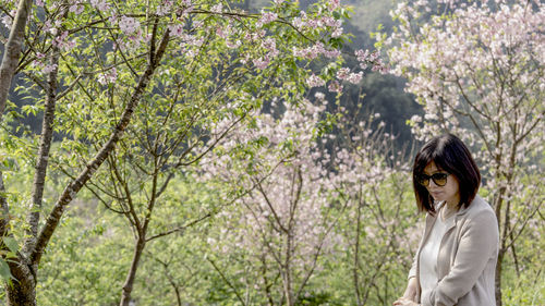 Woman standing by plants against trees