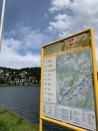 Information sign by lake against sky