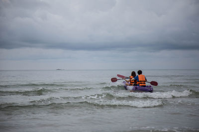 People sitting in sea against sky