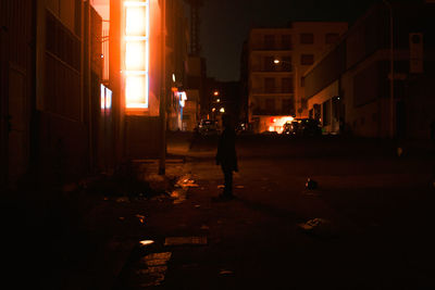 Silhouette woman walking on illuminated street amidst buildings at night