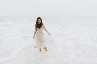 Full length portrait of smiling woman standing on shore at beach