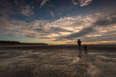 Man standing on beach against sky during sunset