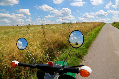 Bicycle parked on field by road against sky